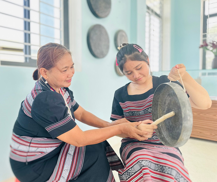 Mrs. Đinh Thị Tuyết (left) instructs Đinh Thị Kim Ngân on how to play the chinh tía (five-gong set). Photo: D.Đ Bà Đinh Thị Tuyết (bìa trái) hướng dẫn em Đinh Thị Kim Ngân cách đánh chinh tía (chiêng 5).